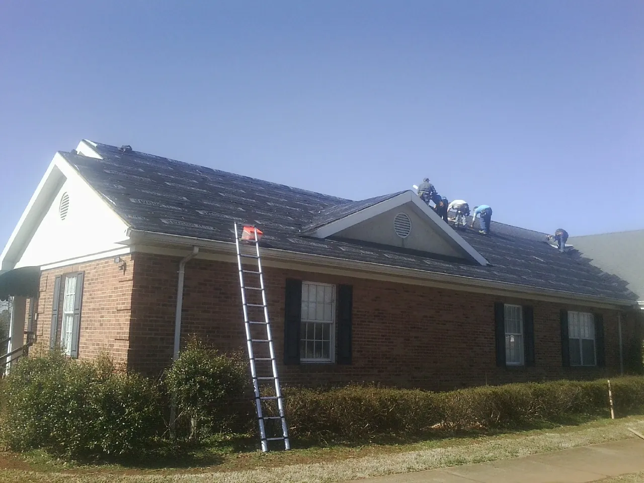 Crew tearing shingles off a brick ranch roof with a ladder set — Emergency Roof Repair work by our crew in Cuba