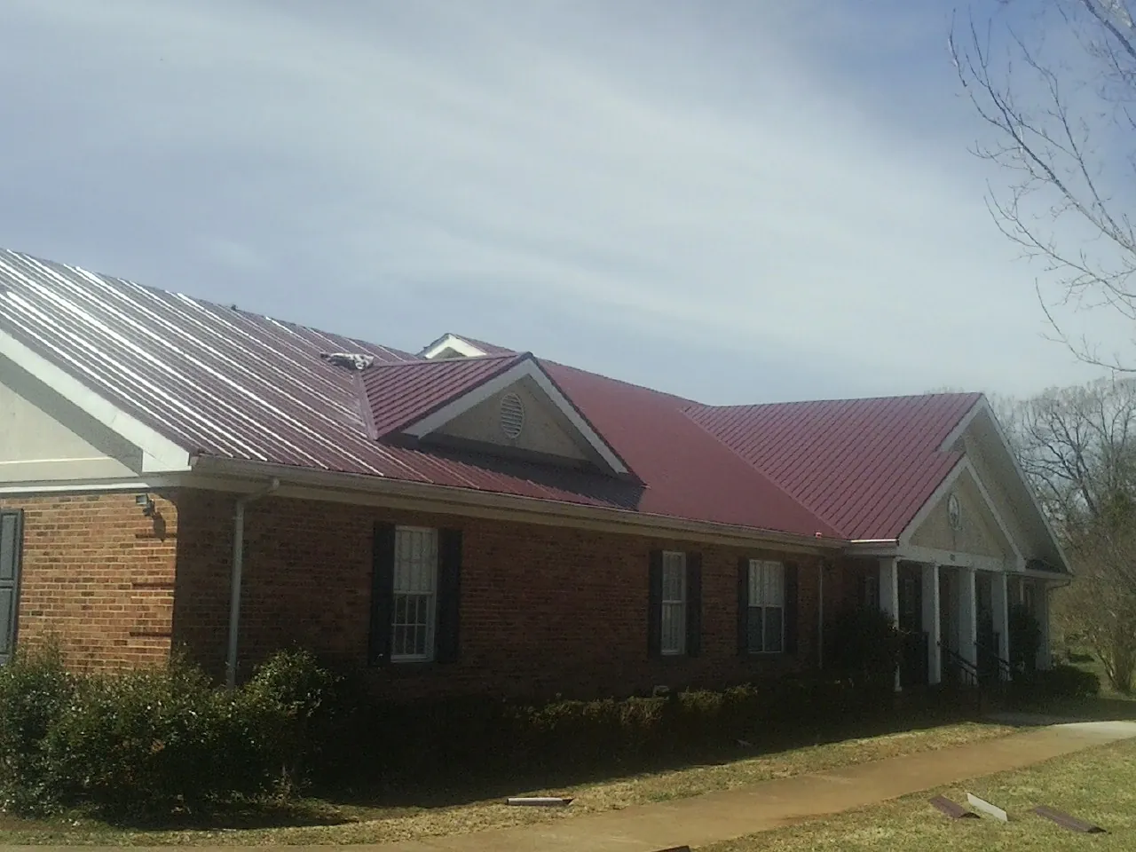 Red metal roof with gabled entries on a long brick building, from a Hail Damage Roof Repair job in Cuba