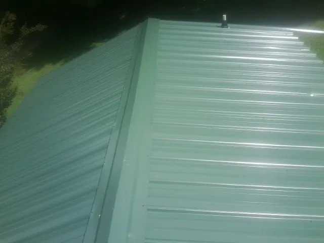 New green metal panels meeting at the ridge of a roof — Flat Roof Repair work by our crew in Cuba